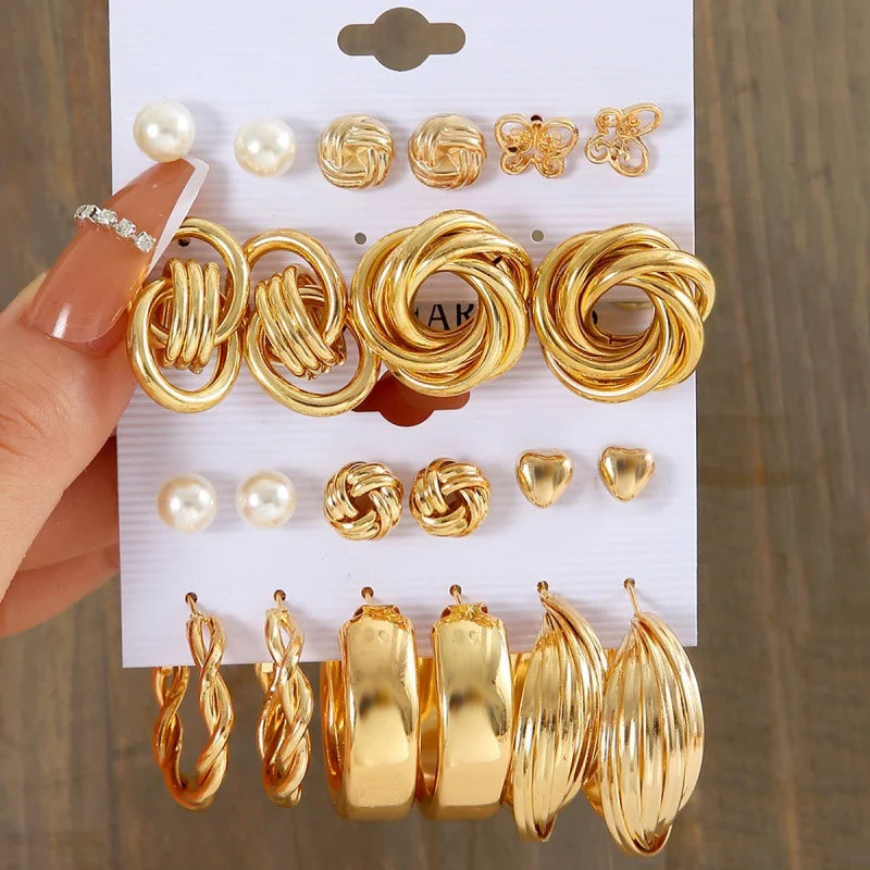 Set of gold earrings on a display card held by a hand.