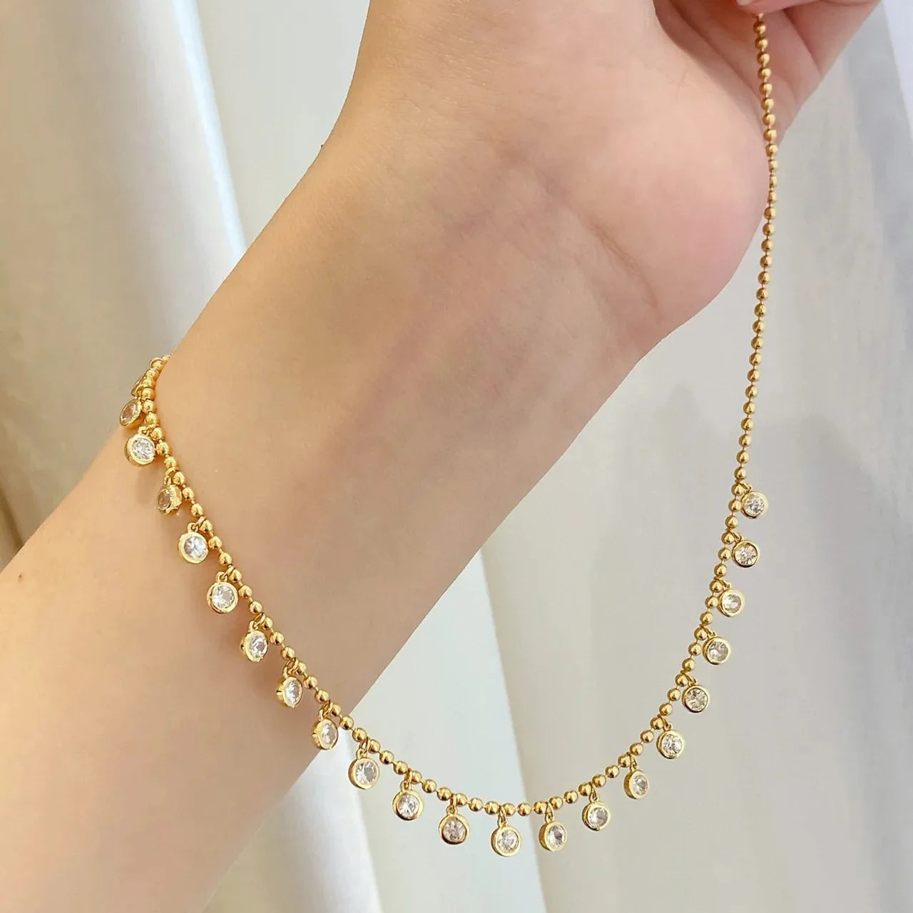 Gold necklace with small crystals on a person's wrist against a light background