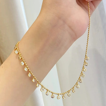 Gold necklace with small crystals on a person's wrist against a light background