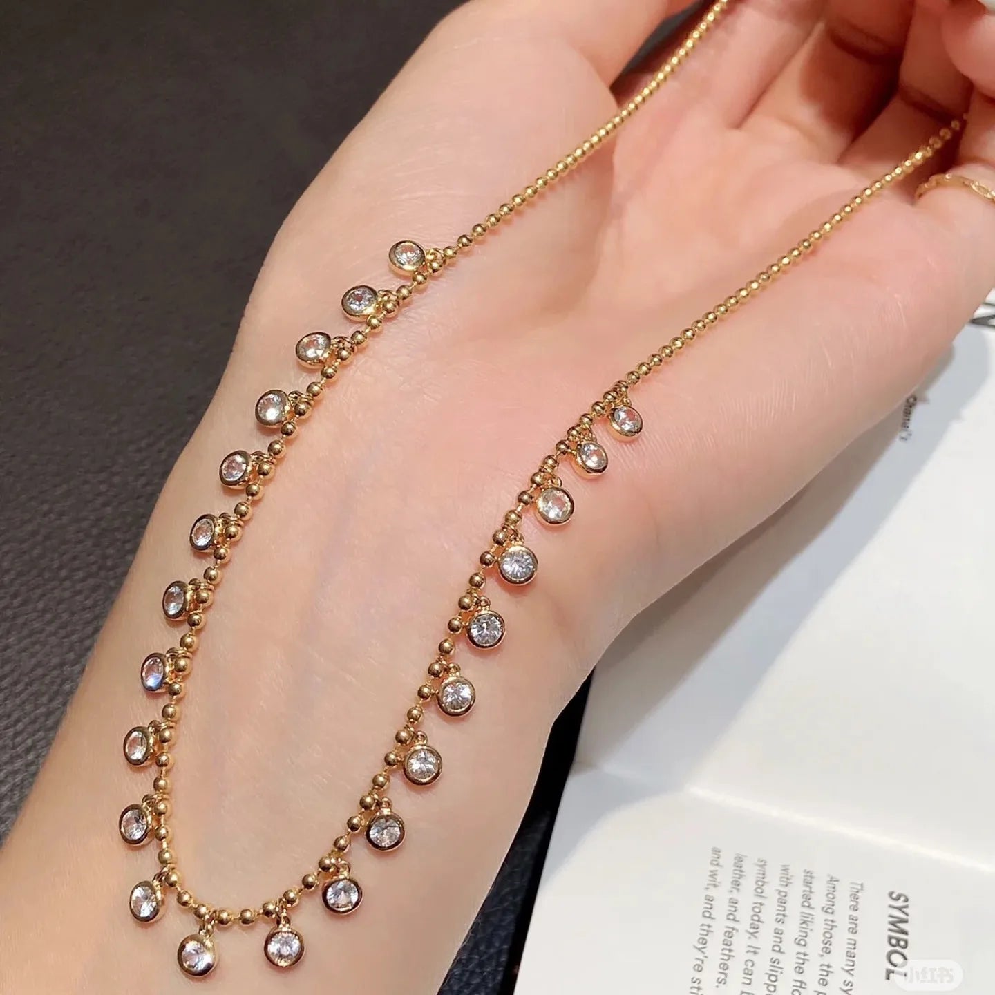 Gold bracelet with small beads on a wrist against a neutral background