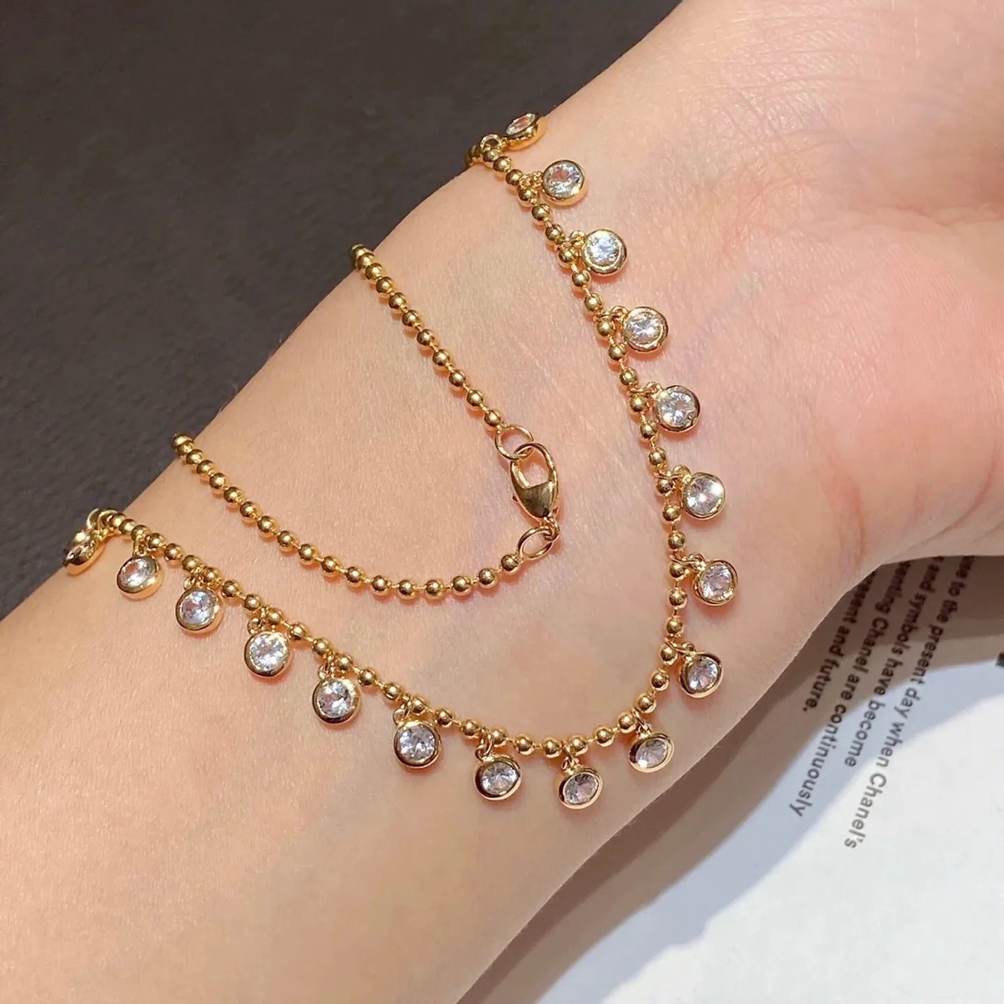 Gold anklets with small crystals on a wrist against a neutral background