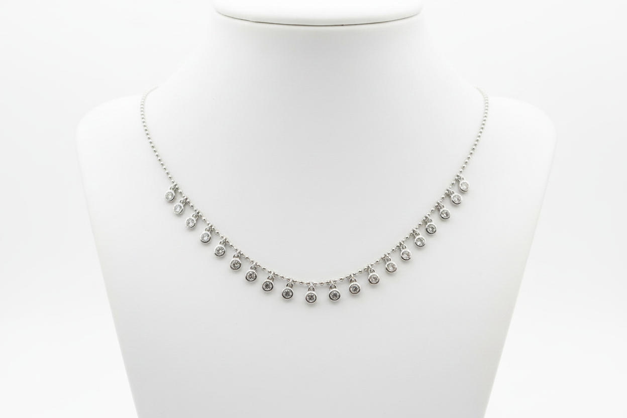 A silver-toned necklace with small dangling round charms, displayed on a white neck mannequin against a white background.