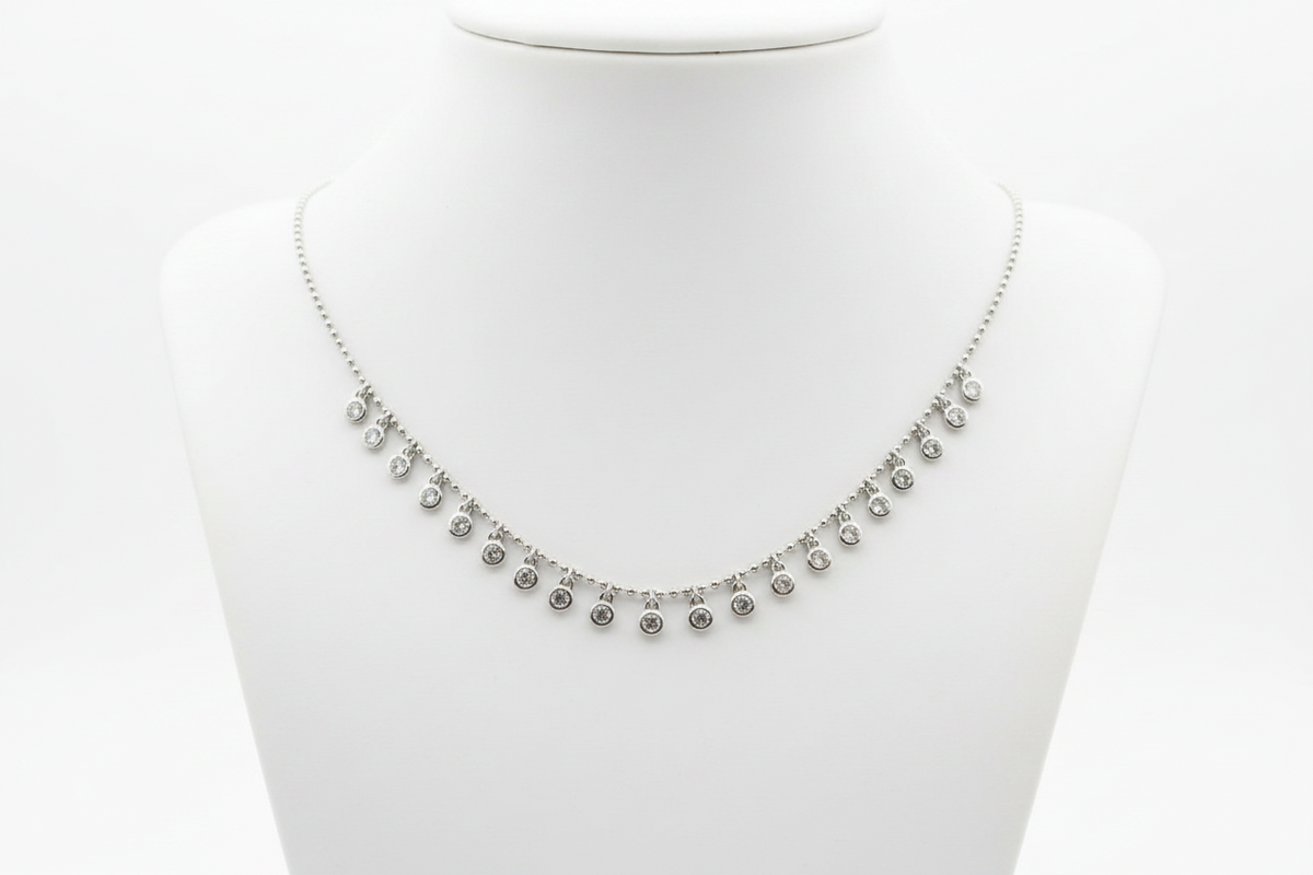 A silver-toned necklace with small dangling round charms, displayed on a white neck mannequin against a white background.