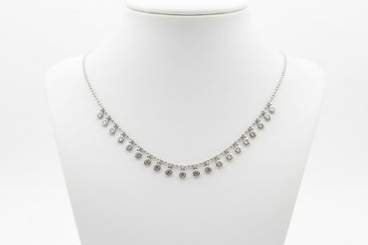 A silver-toned necklace with small dangling round charms, displayed on a white neck mannequin against a white background.