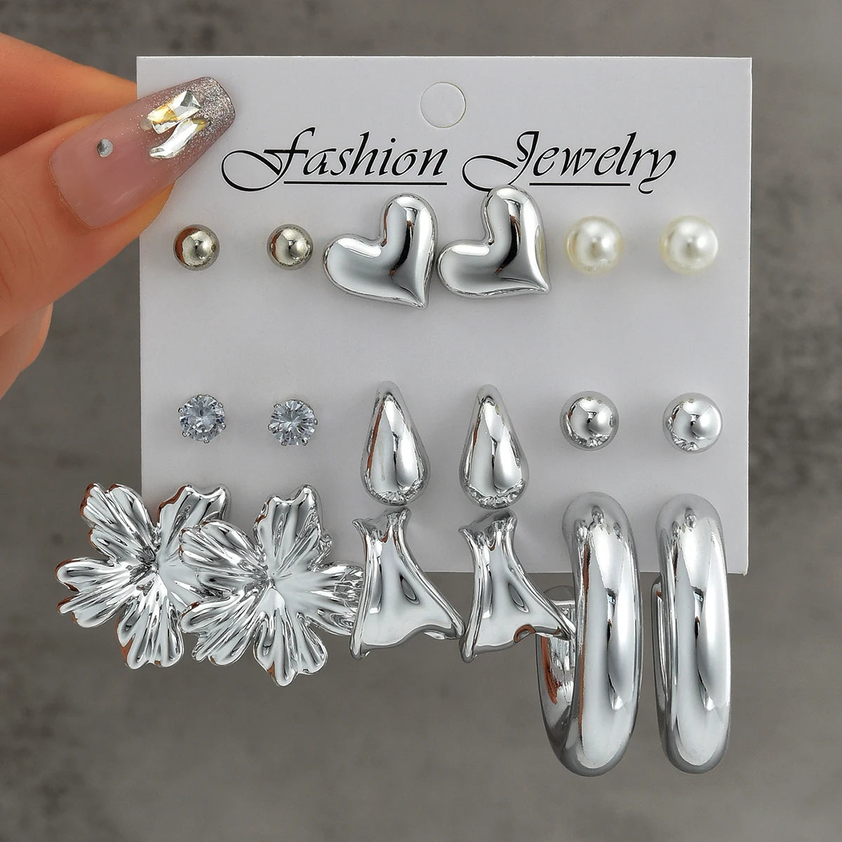 Set of silver earrings on a 'Fashion Jewelry' card held by a hand.