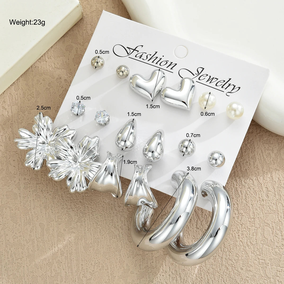 Set of silver earrings on a 'Fashion Jewelry' card with measurements on a beige surface.