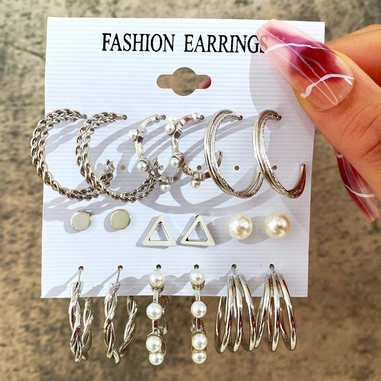 Set of fashion earrings displayed on a card held by a hand.