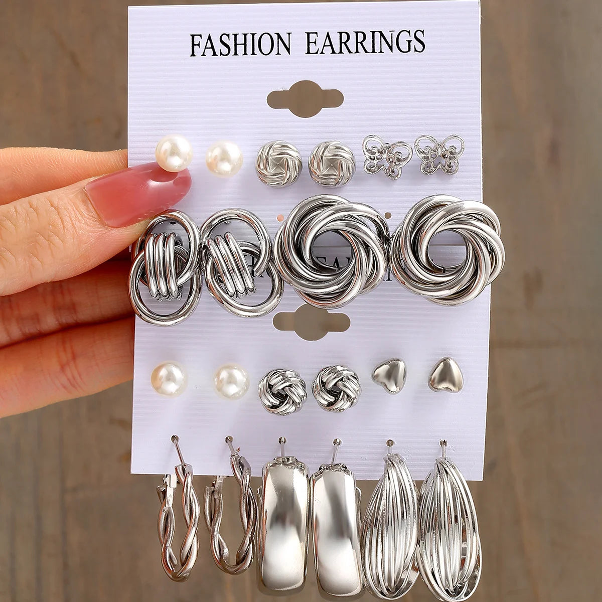 Set of silver fashion earrings on a display card held by a hand.