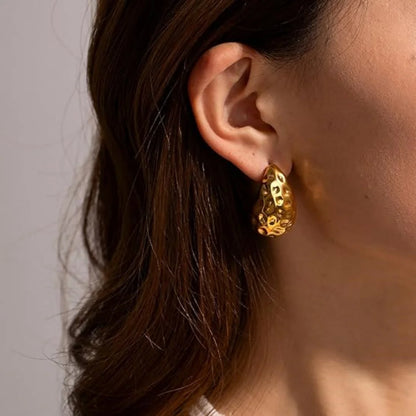 Close-up of a person wearing a gold hoop earring with a neutral background