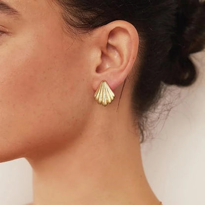 Close-up of a person wearing gold shell-shaped earrings with a neutral background