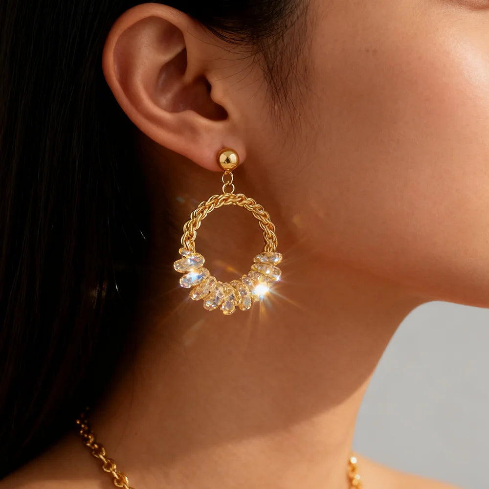 Gold hoop earring with embedded stones worn by a person.