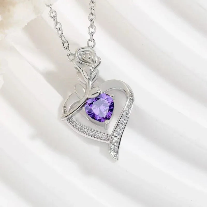 Heart-shaped silver pendant with a purple gemstone on a white background