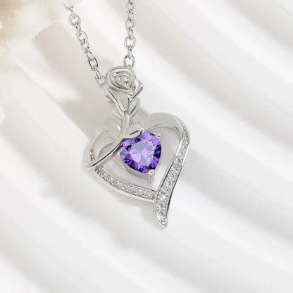 Heart-shaped silver pendant with a purple gemstone on a white background