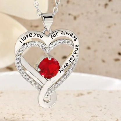 Heart-shaped silver pendant with red gemstone and 'I love you for always and forever' text on a beige background.