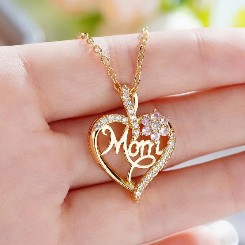 Gold heart-shaped necklace with 'Mom' pendant on a hand