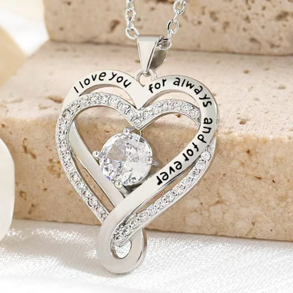Silver heart-shaped pendant with engraved text on a beige surface