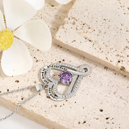 Silver necklace with a purple gemstone on a beige stone surface with flowers.
