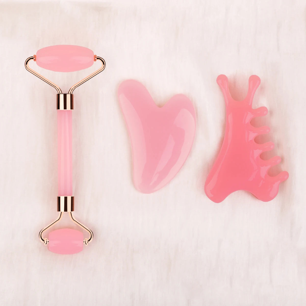 Set of pink facial tools including a roller and two gua sha tools on a white background