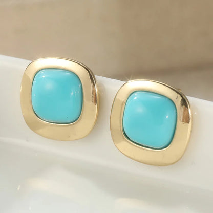 A pair of gold square stud earrings with rounded turquoise blue centers, resting on a white surface.