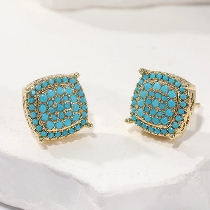 A pair of gold-toned square stud earrings with a layered circular arrangement of bright turquoise blue stones, displayed on a white textured surface.