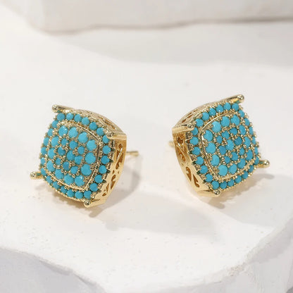 A pair of gold-toned stud earrings with a square cushion-cut design, decorated with a dense arrangement of small turquoise blue stones and accented with tiny clear crystals, displayed on a white textured surface.