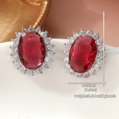 A pair of oval red gemstone stud earrings with silver-toned halo settings, shown on a white surface with overlaid size and weight measurements.