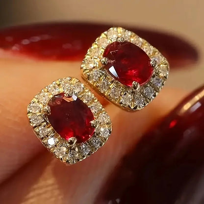 A pair of gold square stud earrings with oval red gemstones 