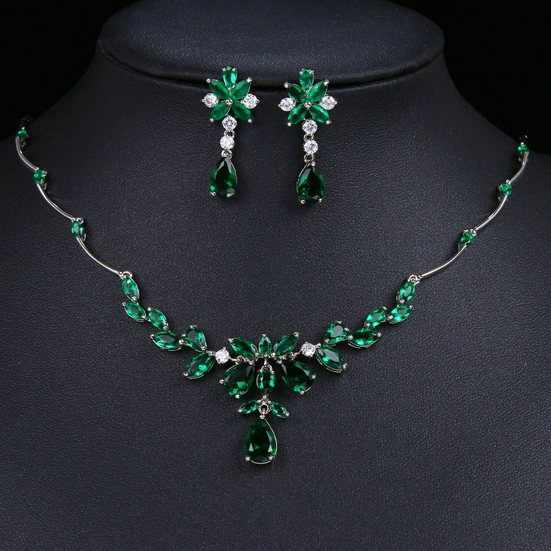 Emerald green gemstone jewelry set including a necklace and matching earrings displayed on a black jewelry bust. The set features silver-tone metal settings with clear rhinestones and green teardrop and marquise-cut stones.