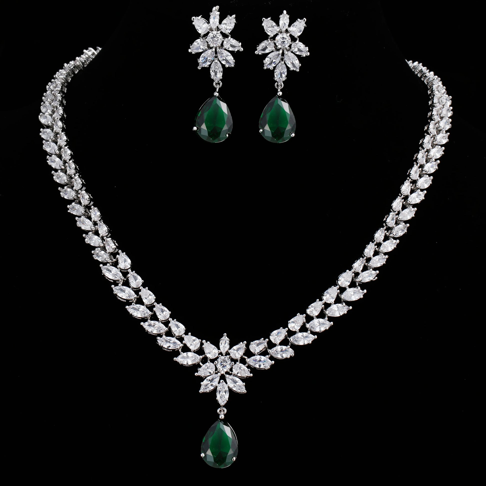 A silver-tone jewelry set featuring a necklace and matching earrings, decorated with clear marquise and round stones, with deep green teardrop gemstone drops, displayed on a solid black background.