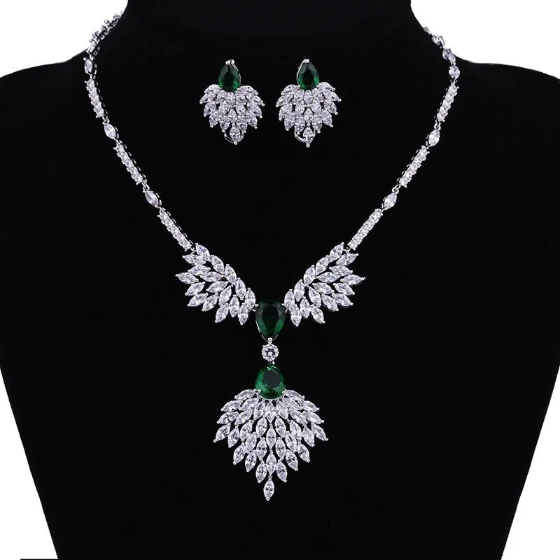 A silver-tone jewelry set displayed on a black mannequin bust, featuring a necklace and matching earrings with leaf-shaped crystal clusters and green gemstone accents.