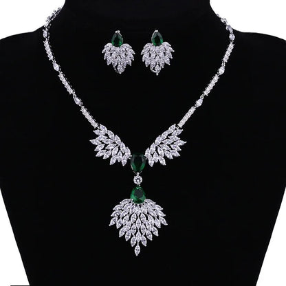 A silver-tone jewelry set displayed on a black mannequin bust, featuring a necklace and matching earrings with leaf-shaped crystal clusters and green gemstone accents.