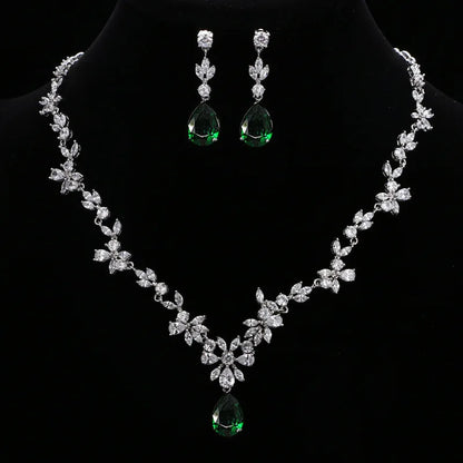 A silver-tone floral necklace and matching drop earrings displayed on a black jewelry bust. The necklace and earrings are set with clear stones and feature green teardrop gemstones at the center and bottom.