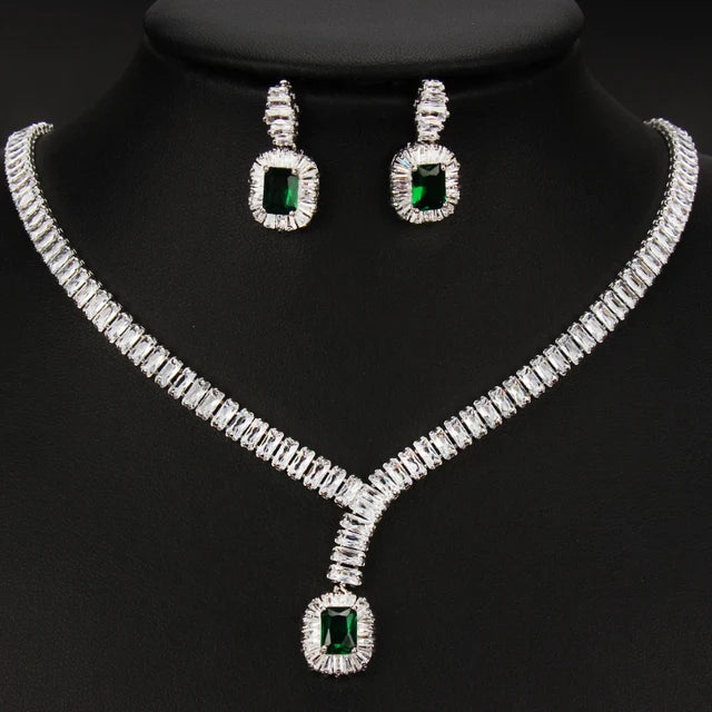 Silver-tone jewelry set featuring a necklace and matching earrings with rectangular green gemstones surrounded by clear stones, displayed on a black mannequin bust.