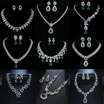 A collage showing eight different styles of women's jewelry sets, including necklaces, earrings, and rings, made of silver-toned metal with clear stones and green emerald-cut gemstones, displayed on black mannequins against a black background.