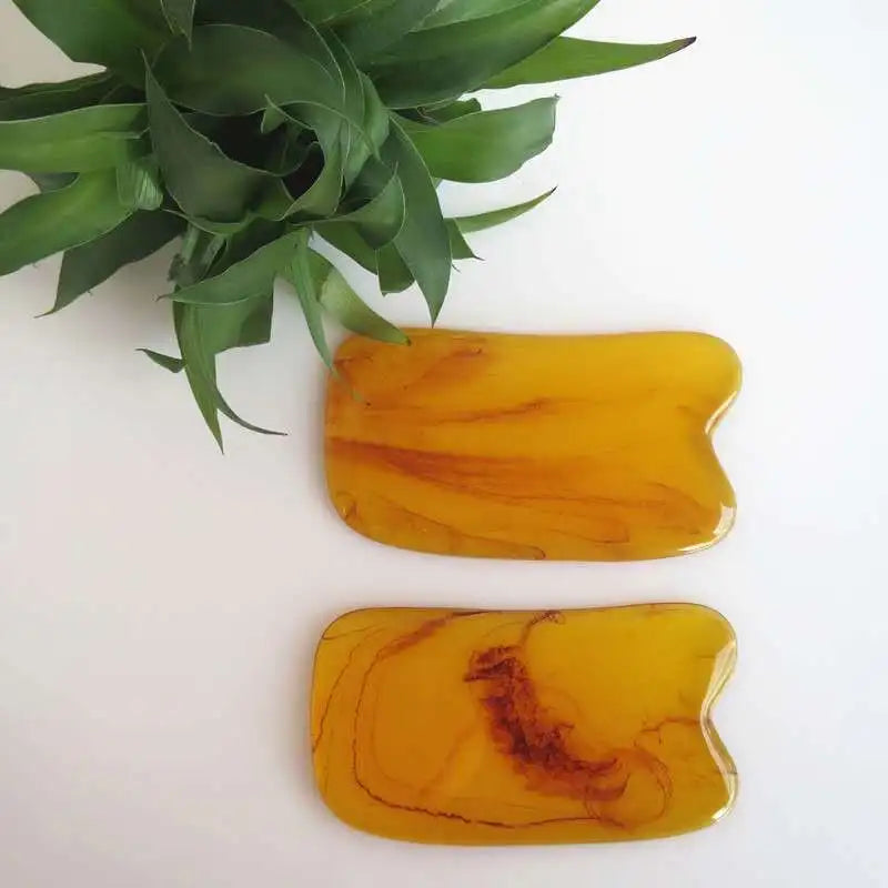 Two amber-colored stone tools on a white surface with green leaves in the corner.