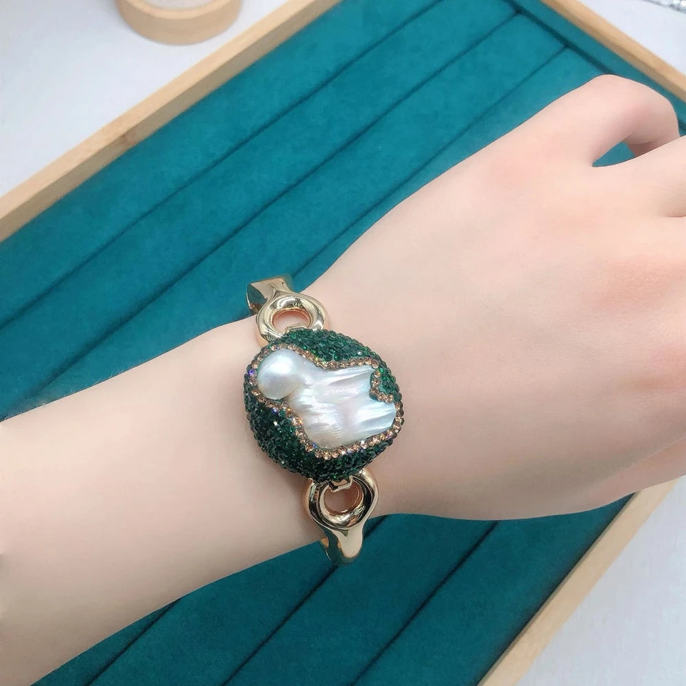 Hand wearing a bracelet with a pearl-like charm on a teal background