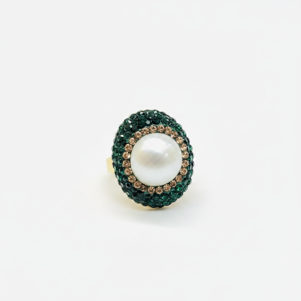 An oval ring featuring a large white pearl center surrounded by a halo of dark green pavé stones and a border of small brown stones, set on a plain white background.
