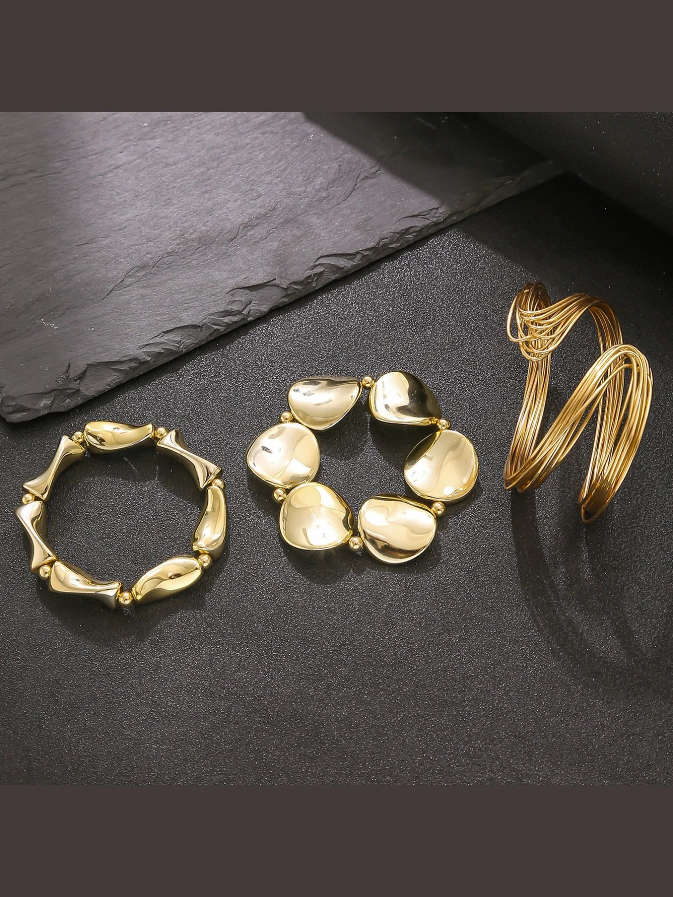 Three gold bracelets on a dark slate surface