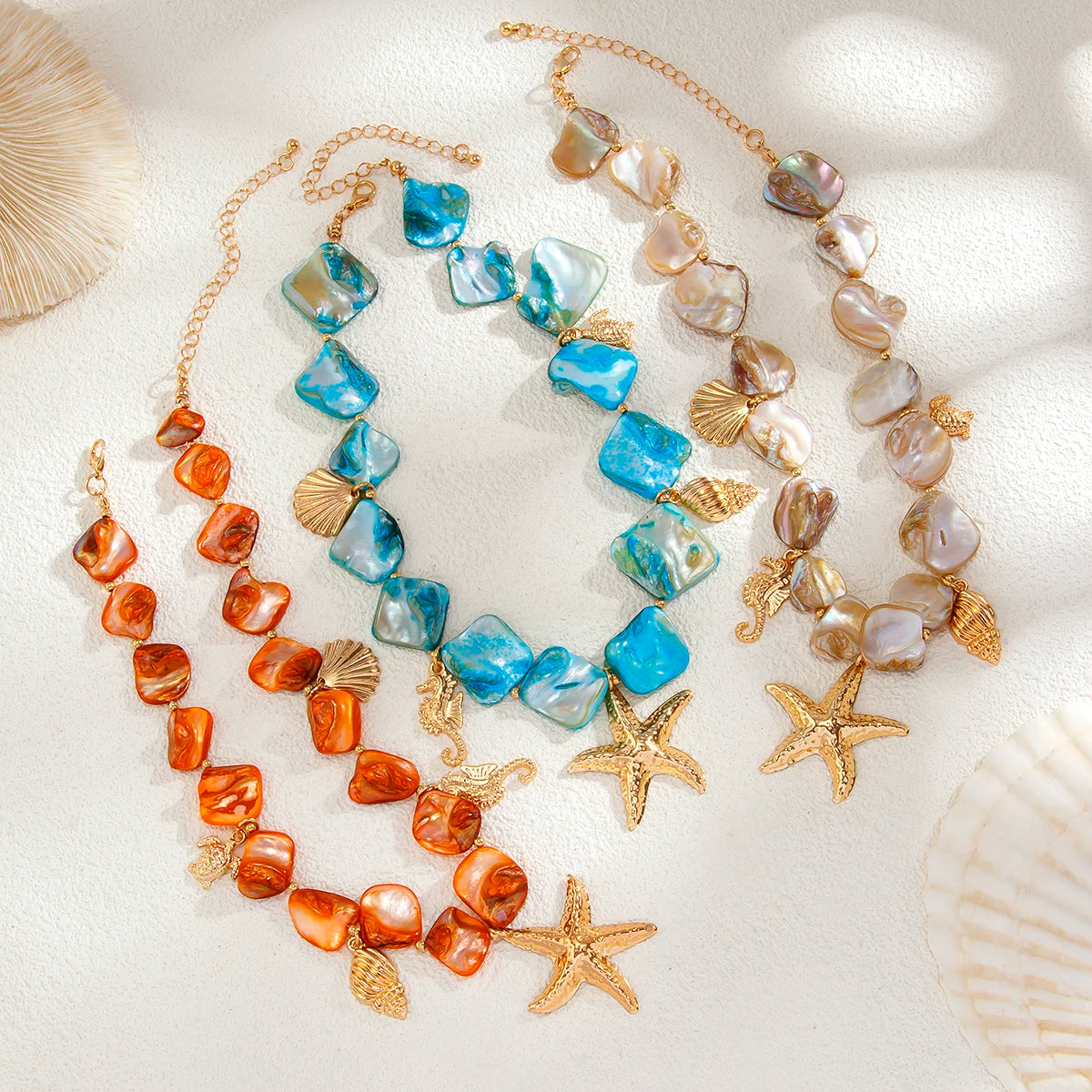 Three necklaces with starfish charms on a white surface with shells.