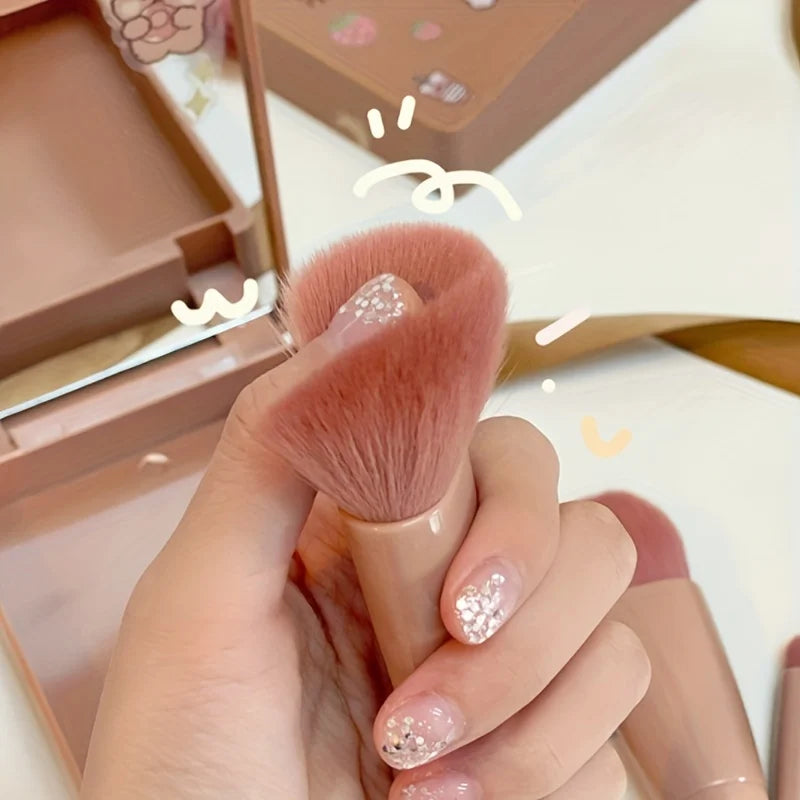 Makeup brush held by a hand with glittery nails, against a blurred makeup product background.