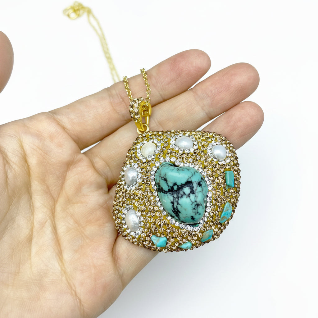 Gold necklace with a turquoise pendant held in a hand against a light blue background