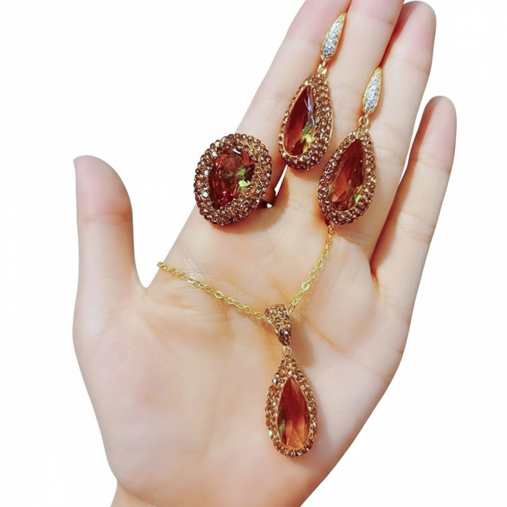 A gold-toned jewelry set with a teardrop pendant, matching drop earrings, and an oval ring, displayed on an open hand against a white background.
