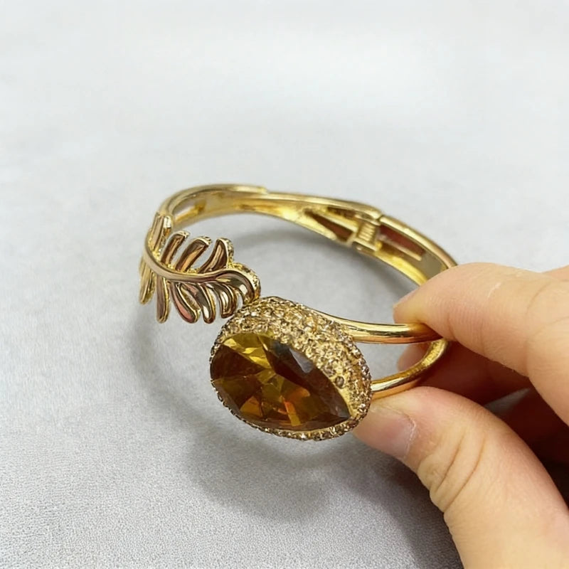 Gold bracelet with a large brown gemstone held by a hand on a light gray background