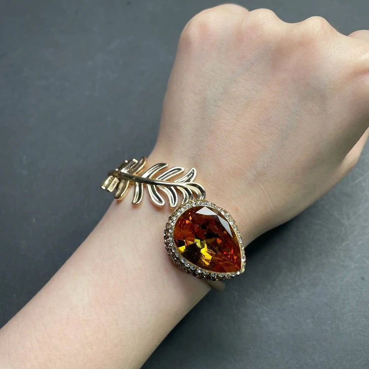 Gold bracelet with a large amber stone on a wrist against a dark background