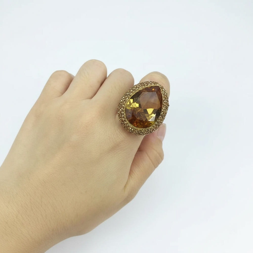 A gold ring with a large teardrop-shaped brown gemstone, worn on a person's finger against a plain white background.