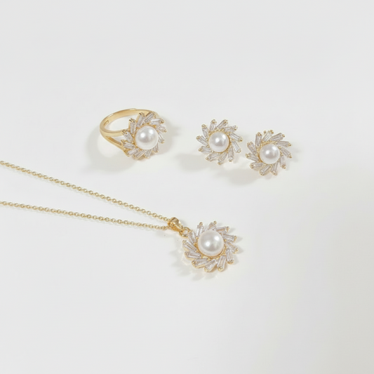 A gold jewelry set featuring a ring, a pendant necklace, and a pair of stud earrings, each designed with a central white pearl surrounded by small clear stones in a sunburst pattern, displayed on a clean white background.